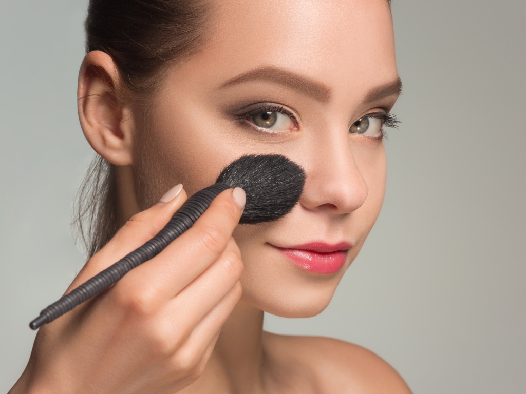 Красивой девушке наносят макияж на лицо кистью 