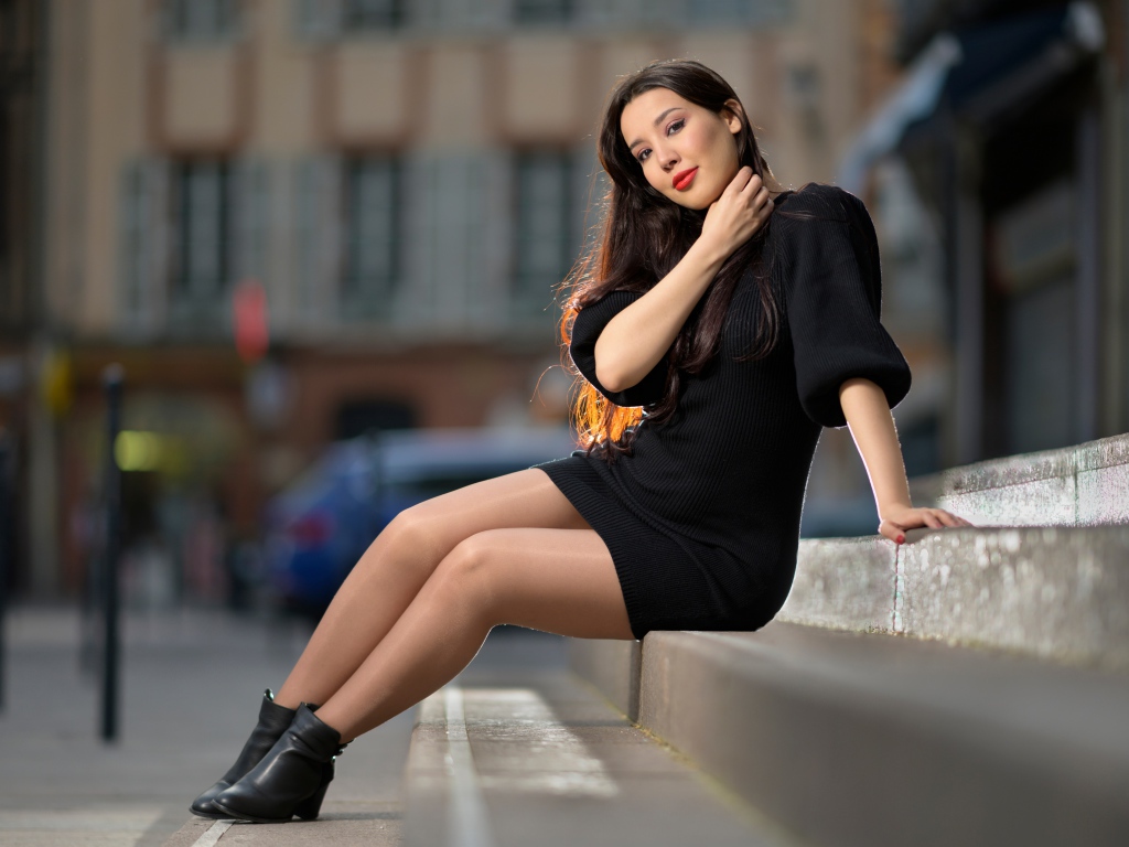 Красивая девушка в черном платье сидит на ступенях