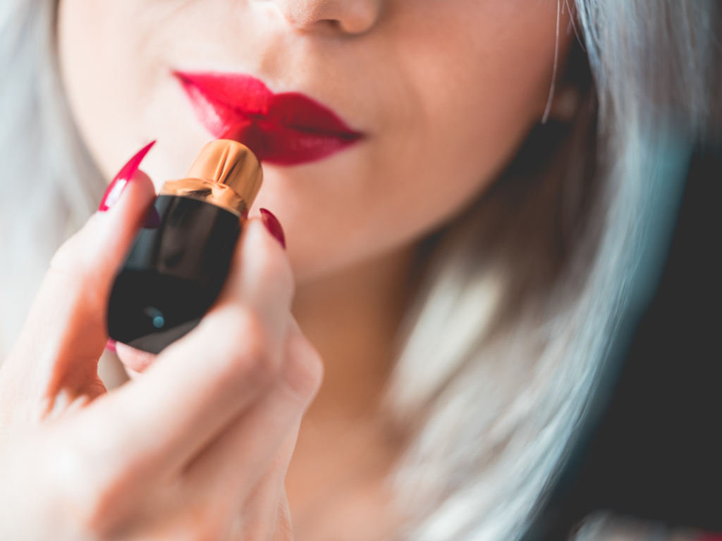 Красивая девушка красит губы красной помадой 