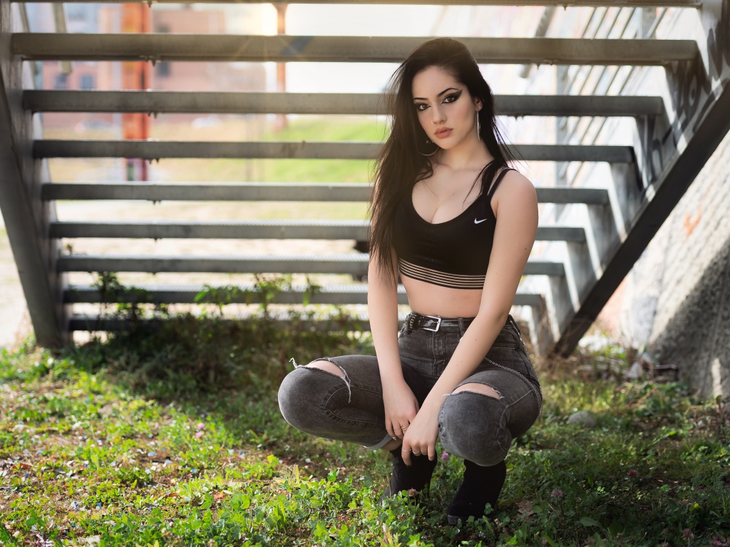 Красивая девушка сидит под лестницей 