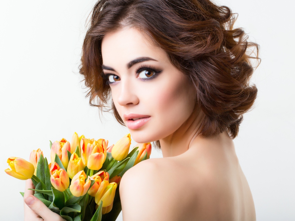Красивая девушка с прической в букетом тюльпанов в руках на белом фоне