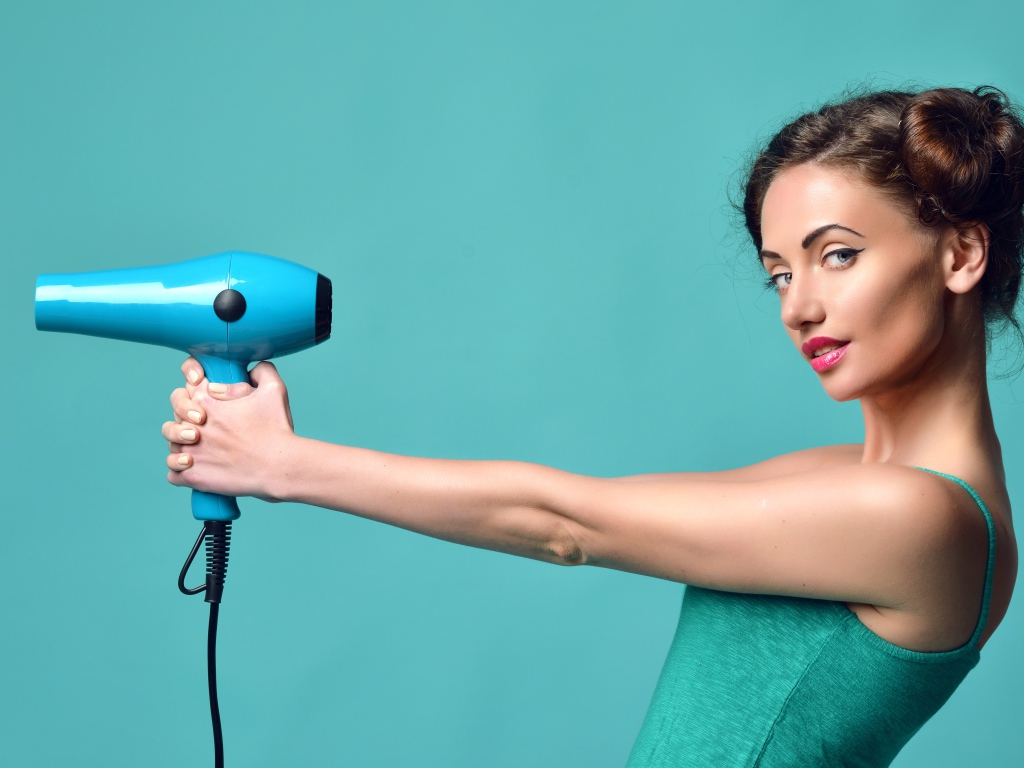 Красивая девушка с феном в руках на голубом фоне