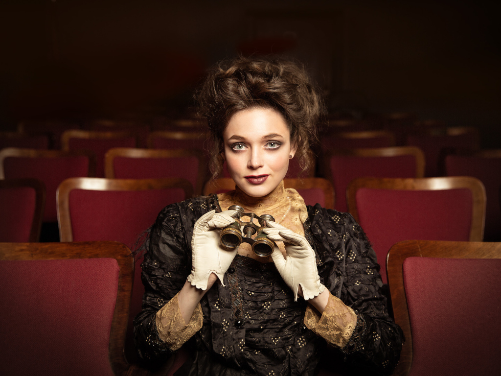 Красивая девушка с биноклем сидит в театре
