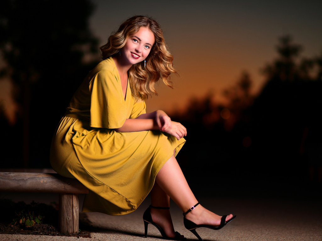 Красивая улыбающаяся девушка в желтом платье сидит на лавке 