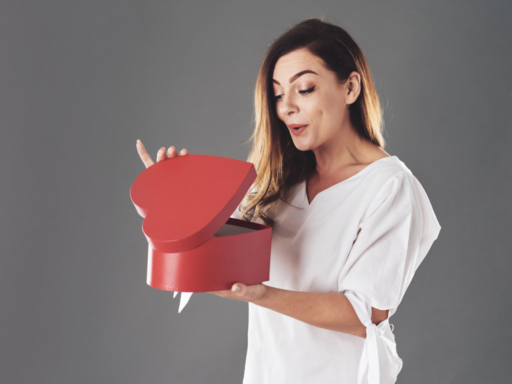 Любопытная девушка смотрит в красную коробку в форме сердца