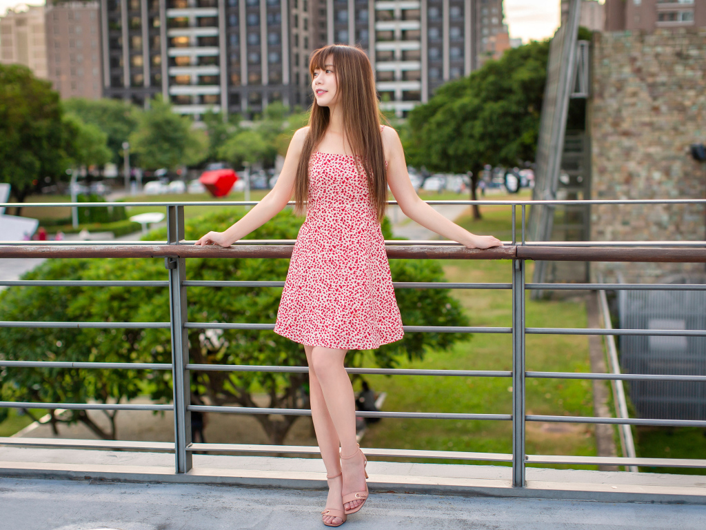 Милая девушка азиатка в платье стоит у перил 