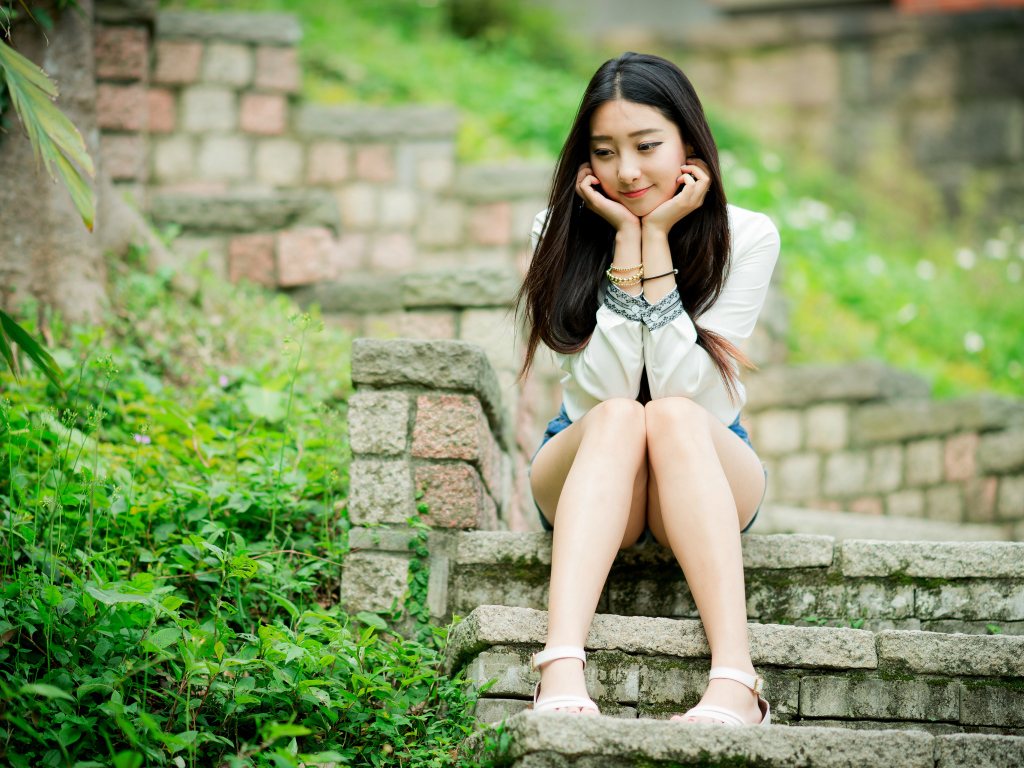 Мечтательная девушка азиатка сидит на ступеньках 