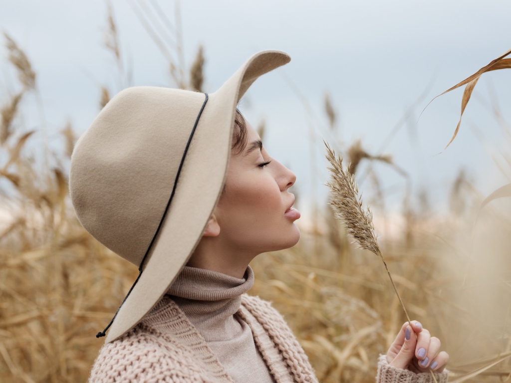 Девушка в шляпе с закрытыми глазами держит колосок 
