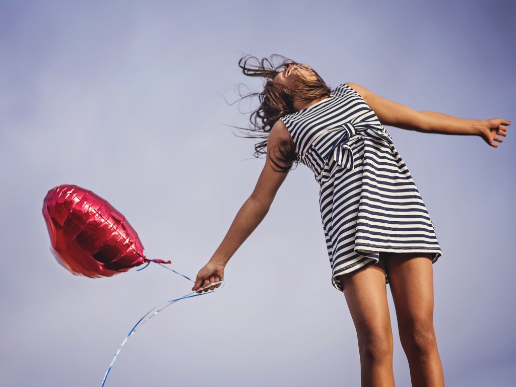 Девушка в полосатом платье прыгает с шариком 