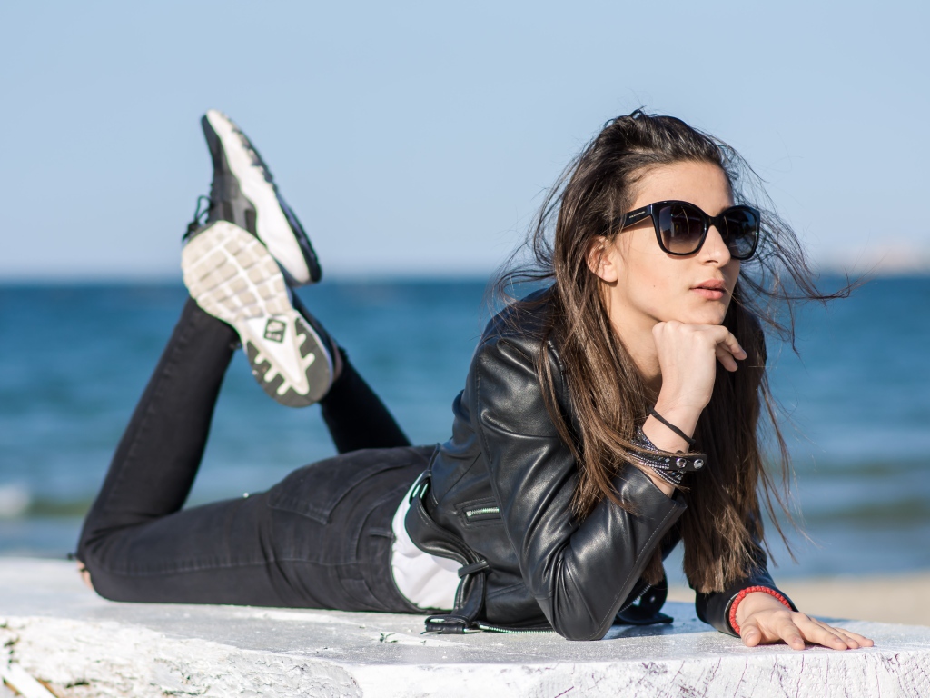 Девушка в черных очках и кожаной куртке на фоне моря