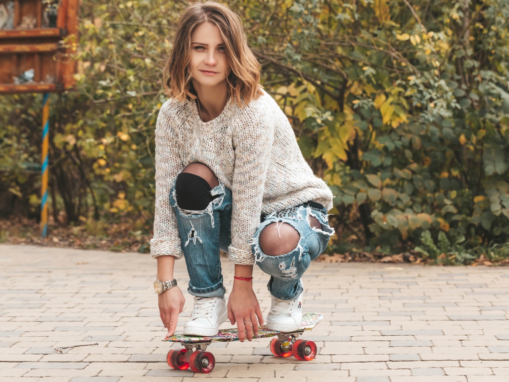 Девушка в рваных джинсах на скейте