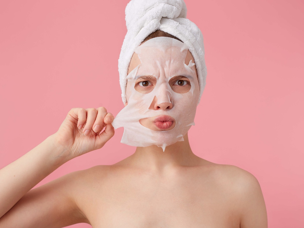 Девушка снимает косметическую маску с лица на розовом фоне 