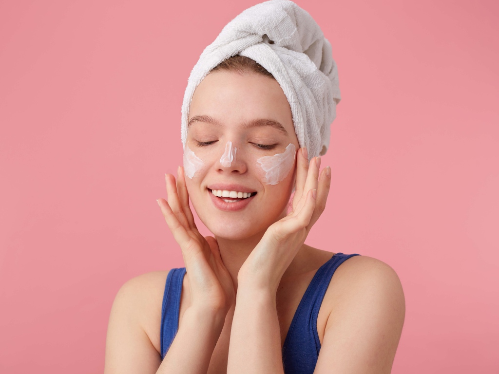 Девушка с полотенцем на голове мажет крем на лицо