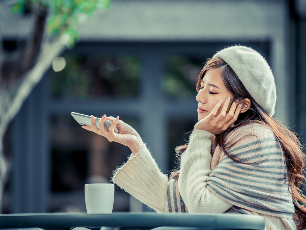 Мечтательная девушка с телефоном сидит в кафе 