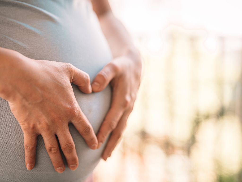 Беременная женщина держит руки на животе 