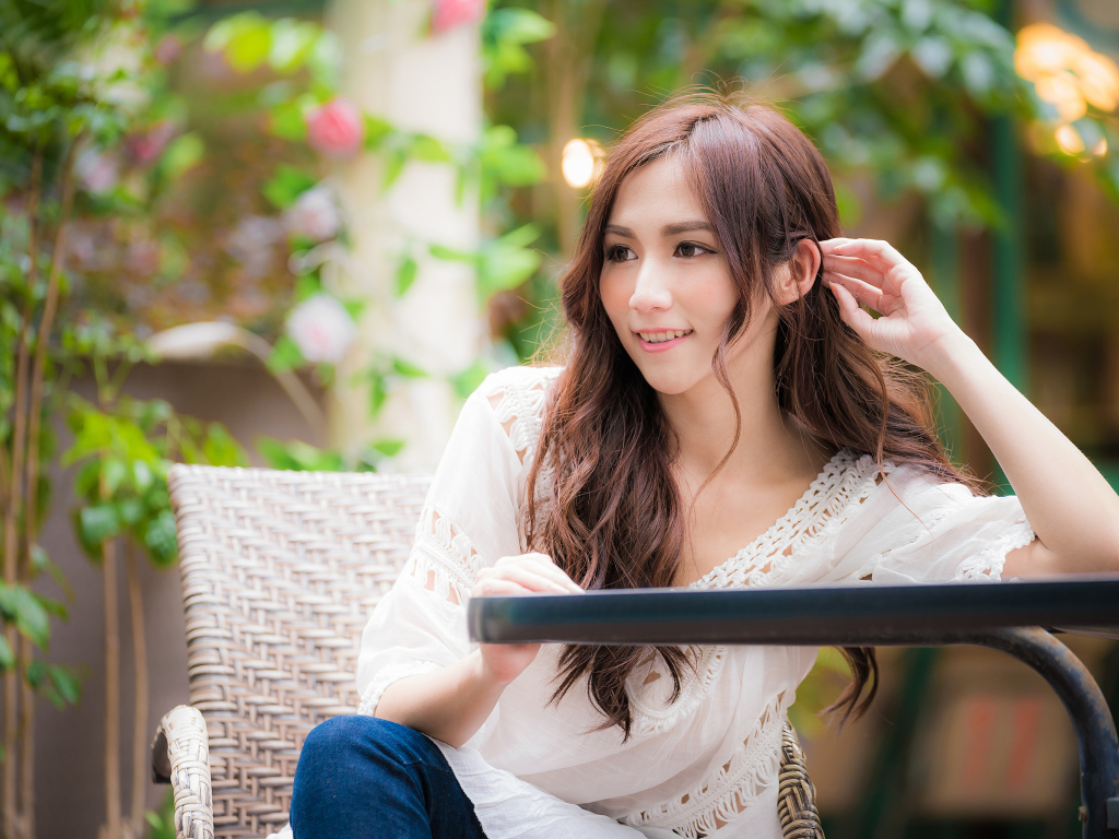 Улыбающаяся девушка азиатка сидит за столом в кафе