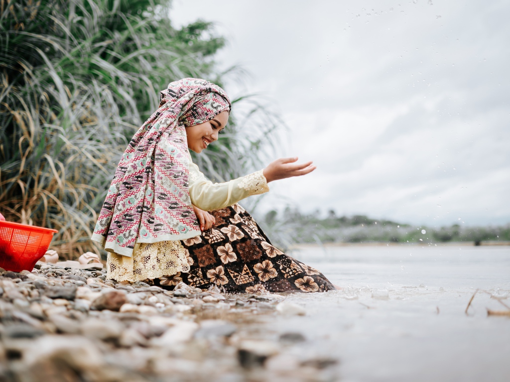 Улыбающаяся девушка азиатка сидит у воды