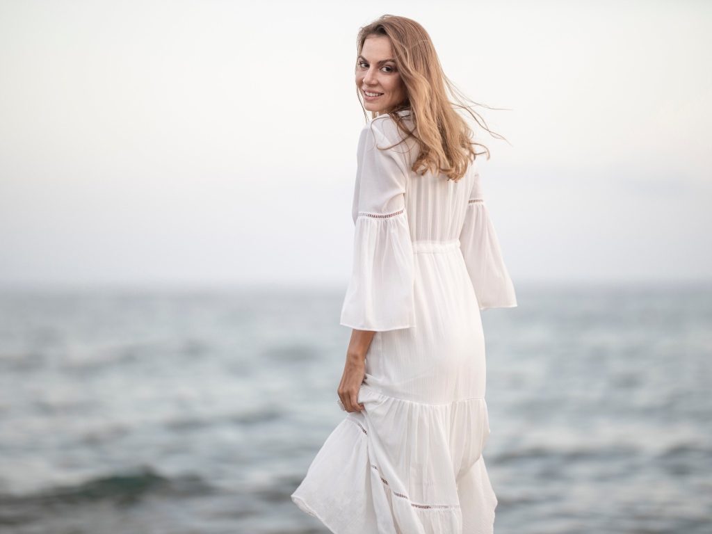 Улыбающаяся девушка в белом платье на фоне моря