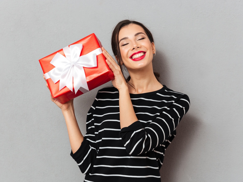 Улыбающаяся девушка с подарком в руках на сером фоне 