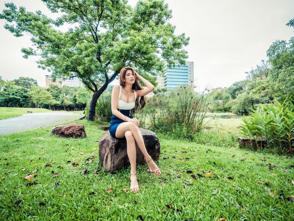 Эффектная девушка азиатка сидит на камне в парке