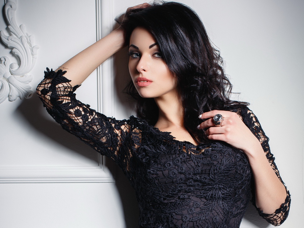 Эффектная брюнетка в черном платье у стены