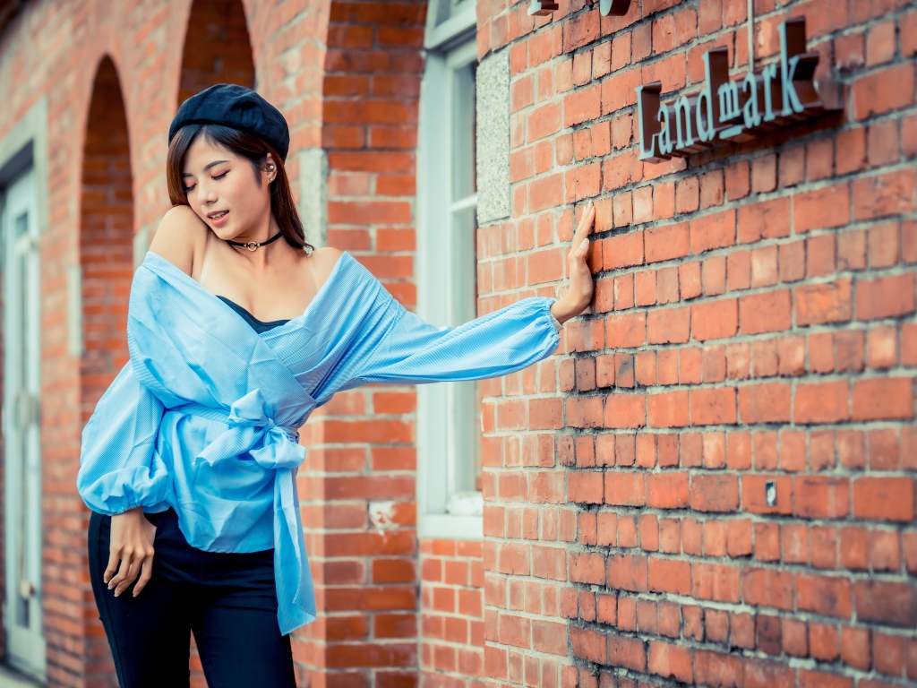 Молодая азиатка в черном берете стоит у стены 