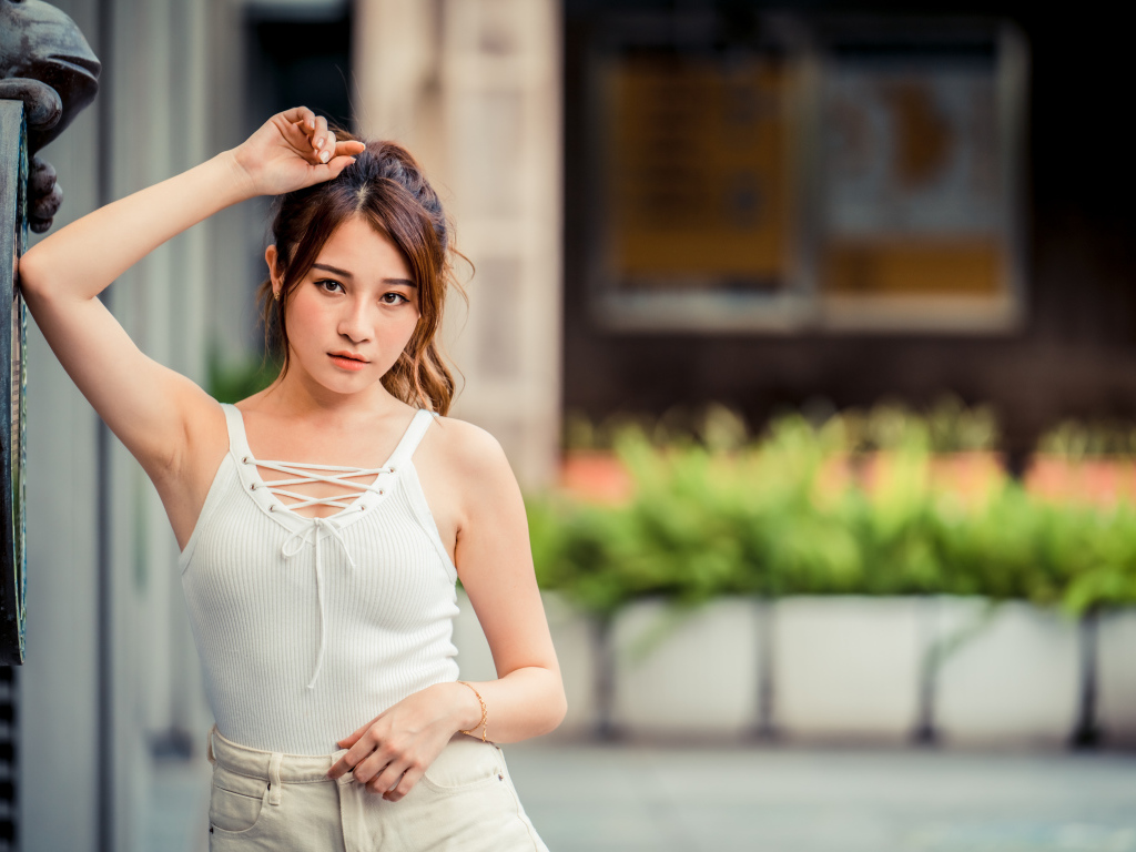 Молодая красивая азиатка в белой майке стоит у ворот