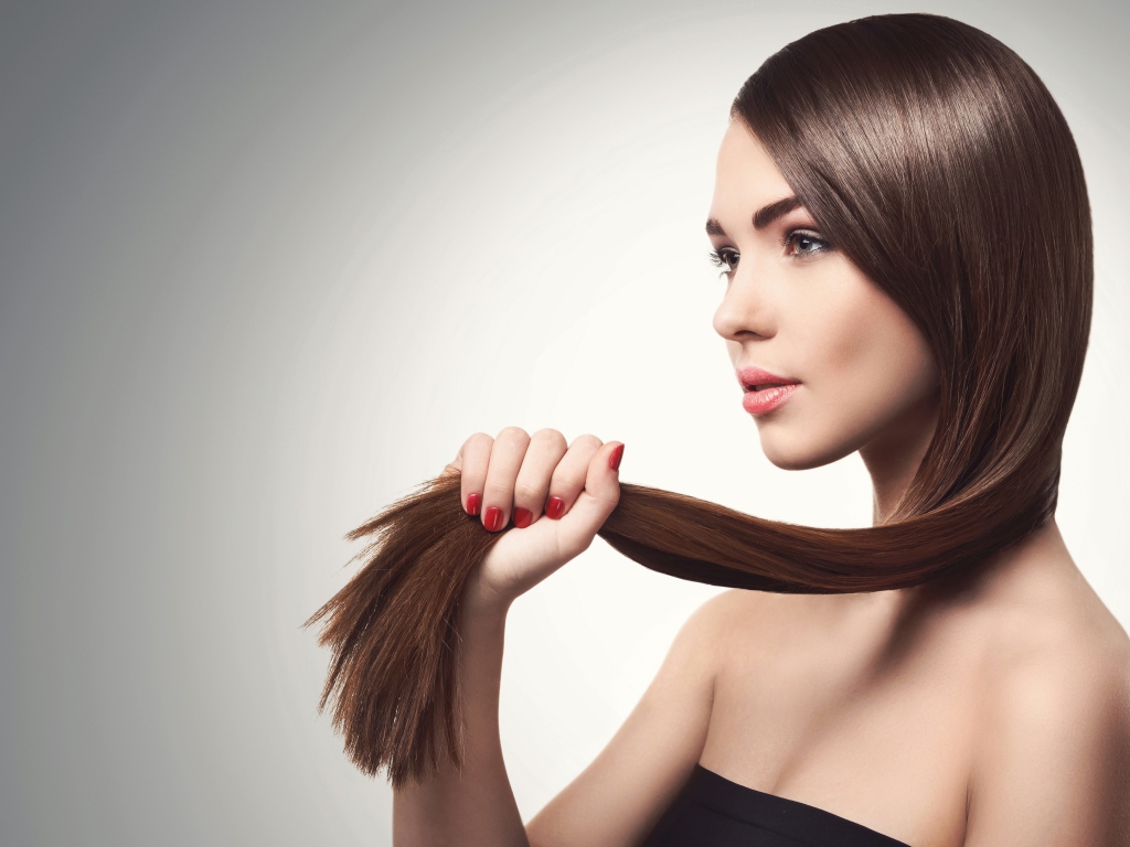 Молодая девушка держит в руках волосы на сером фоне