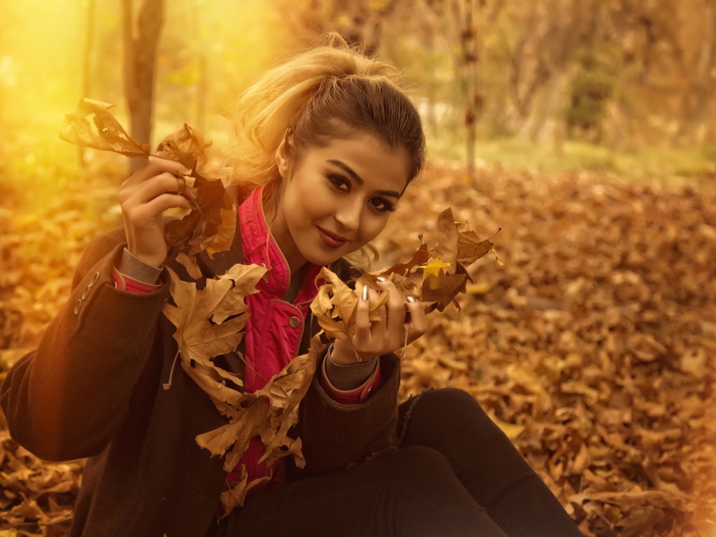 Молодая девушка с опавшими листьями в руках в парке