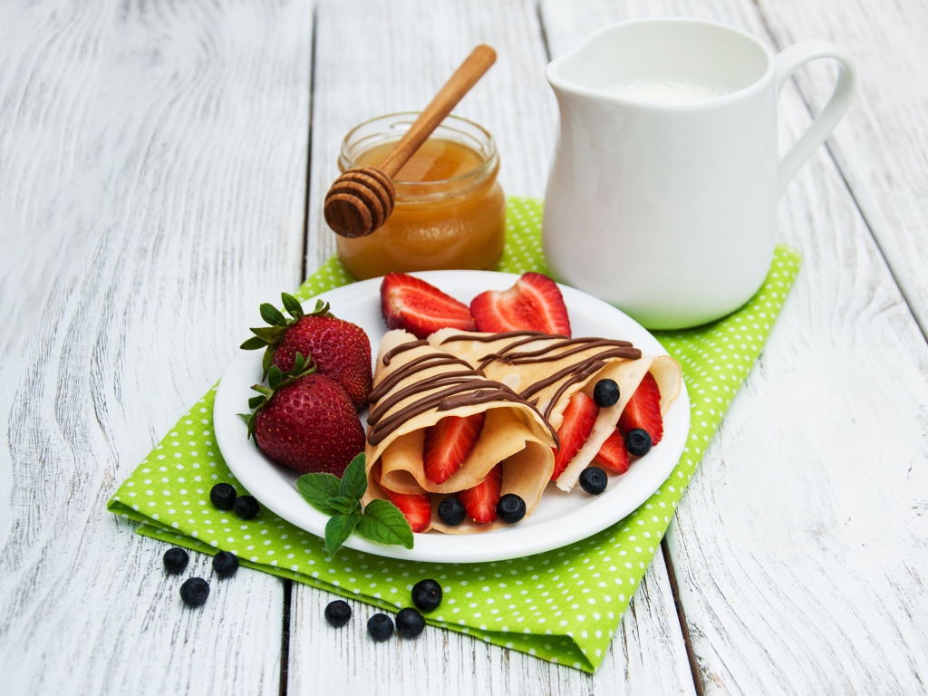 Delicious pancakes with strawberries on a table with milk and honey for Maslenitsa holiday