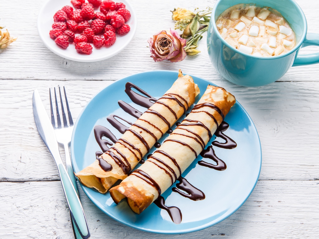 Тонкие блины с шоколадом на столе с ягодами малины и какао 