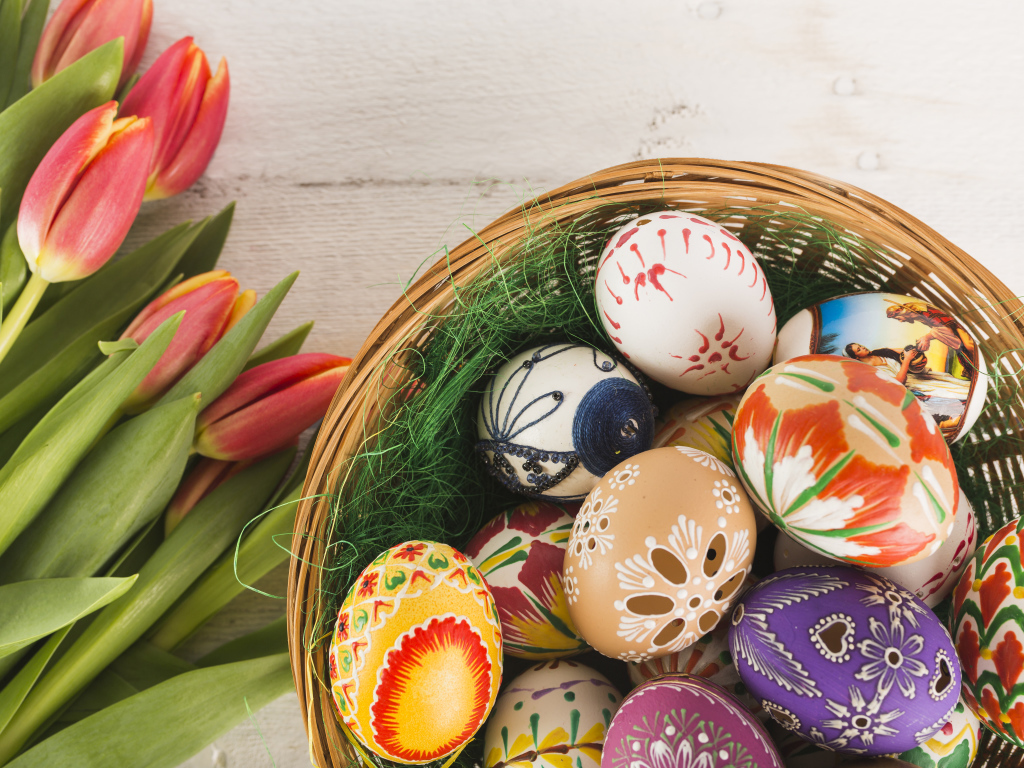Разноцветные крашеные яйца в корзине с букетом тюльпанов на Пасху