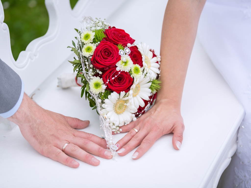 Две руки с обручальными кольцами и свадебным букетом