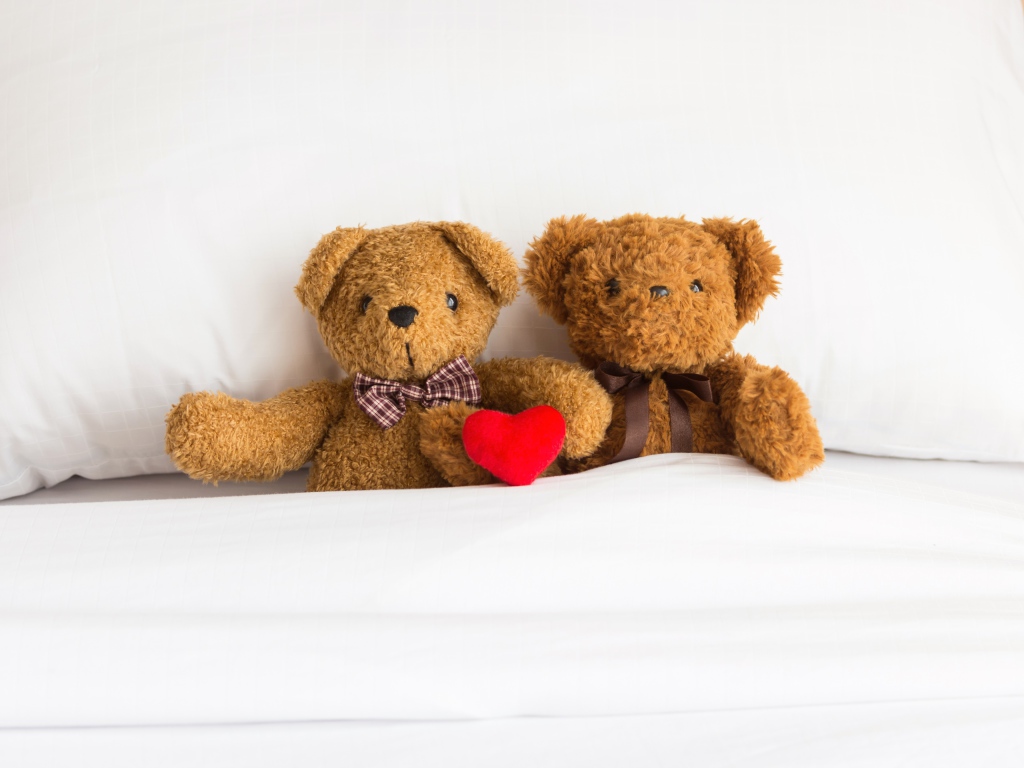 Два медвежонка Тедди лежат на кровати под одеялом 