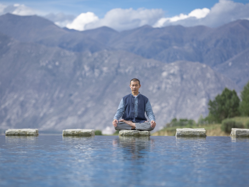 Мужчина азиат в позе лотоса медитирует у воды 