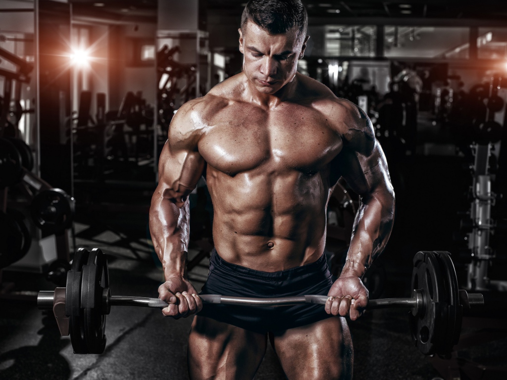 Мускулистый мужчина со штангой в руках в спортзале