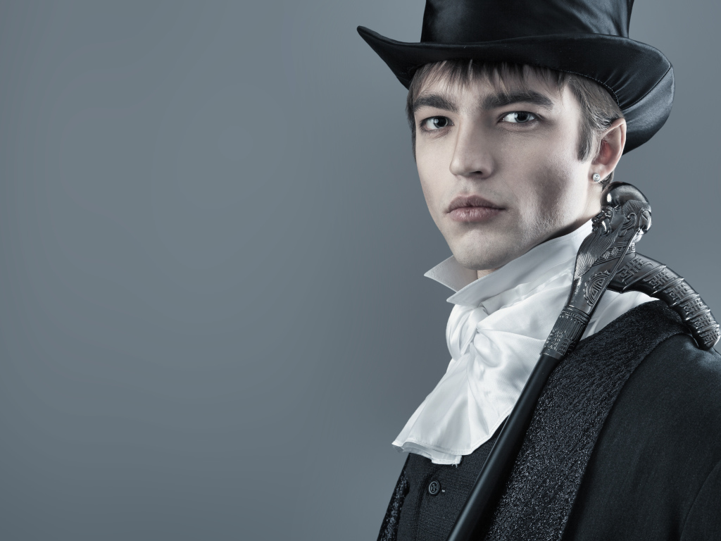 Красивый молодой человек в черном цилиндре и фраке на сером фоне