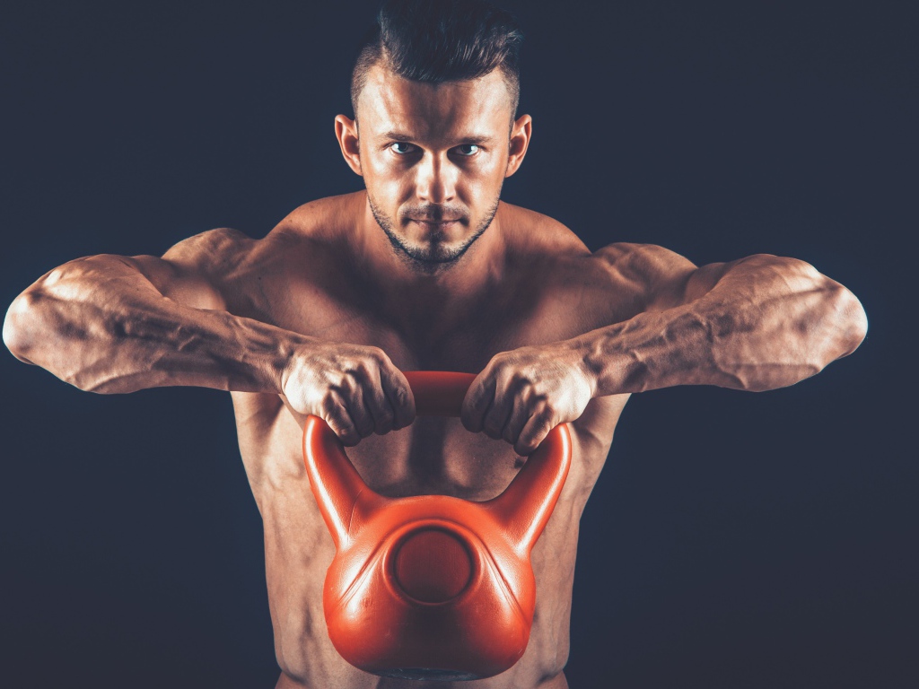 Накаченный парень поднимает тяжелую гирю на черном фоне