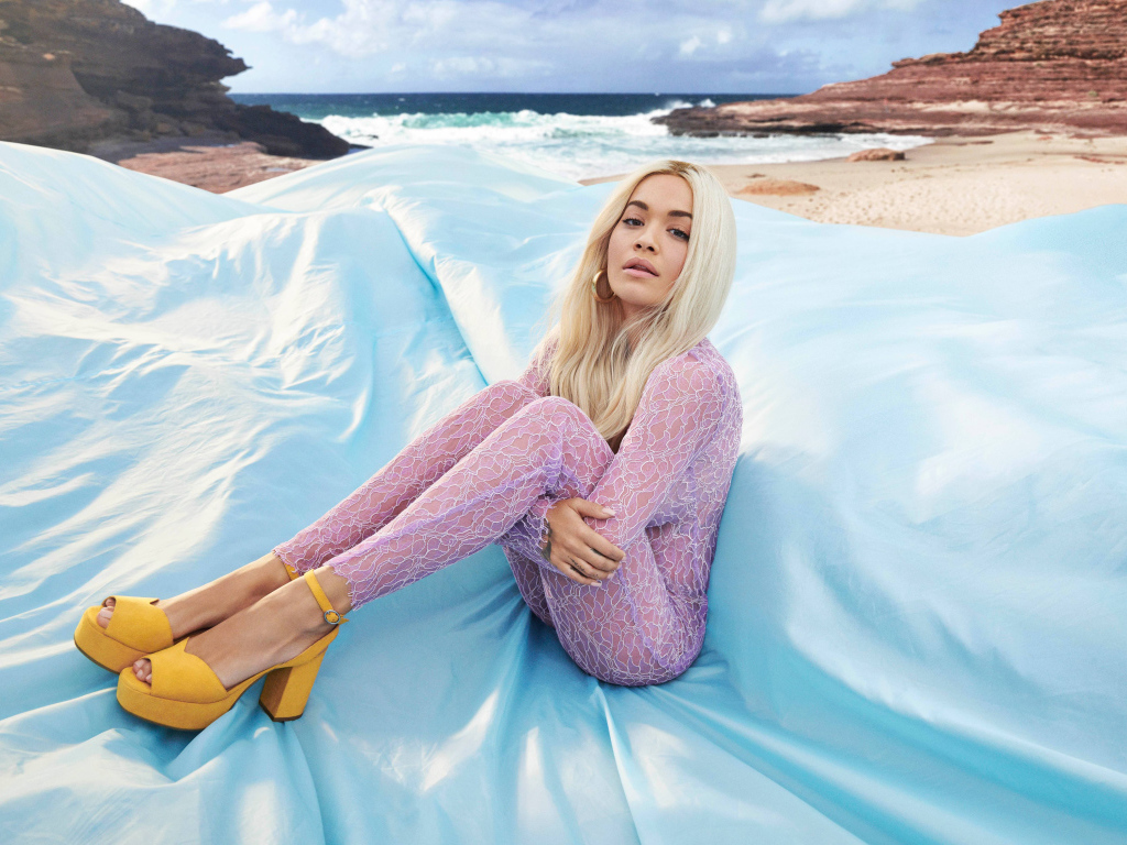 Певица Рита Ора сидит на голубом покрывале у моря