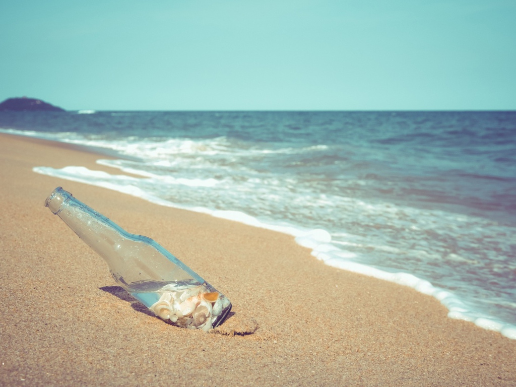 Бутылка с ракушками на песке у моря