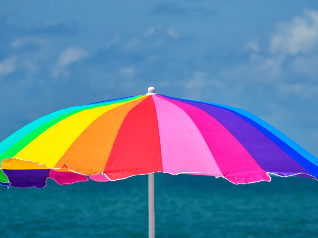 Большой разноцветный пляжный зонт на фоне моря
