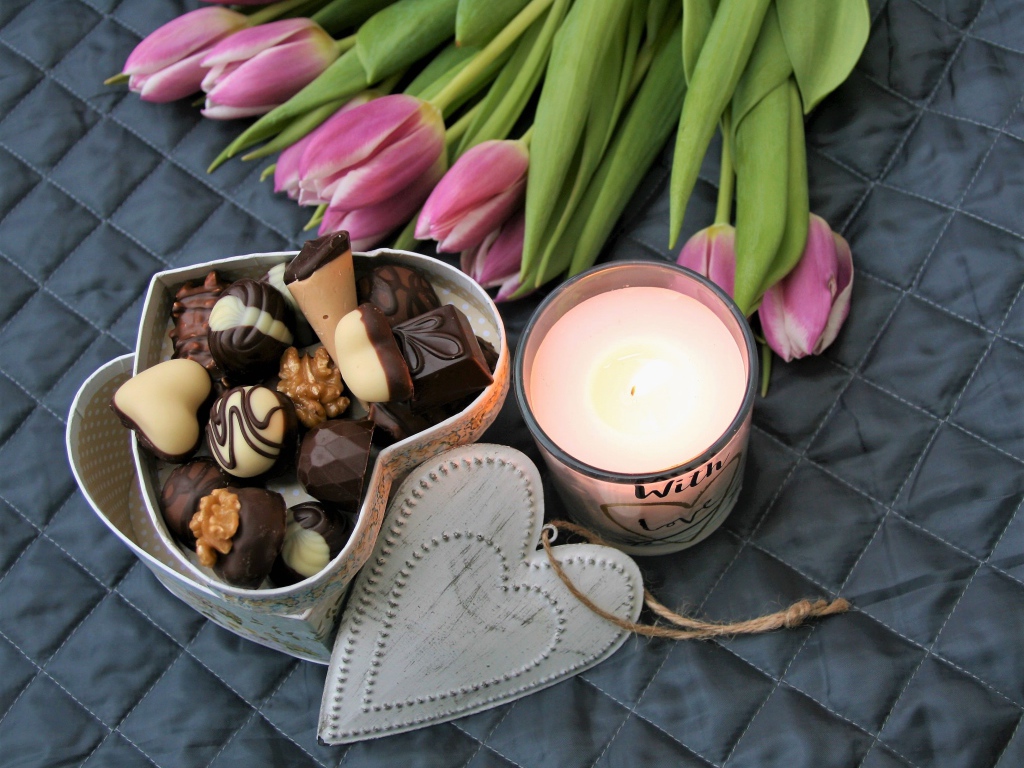 Букет розовых тюльпанов на кровати со свечой и коробкой конфет