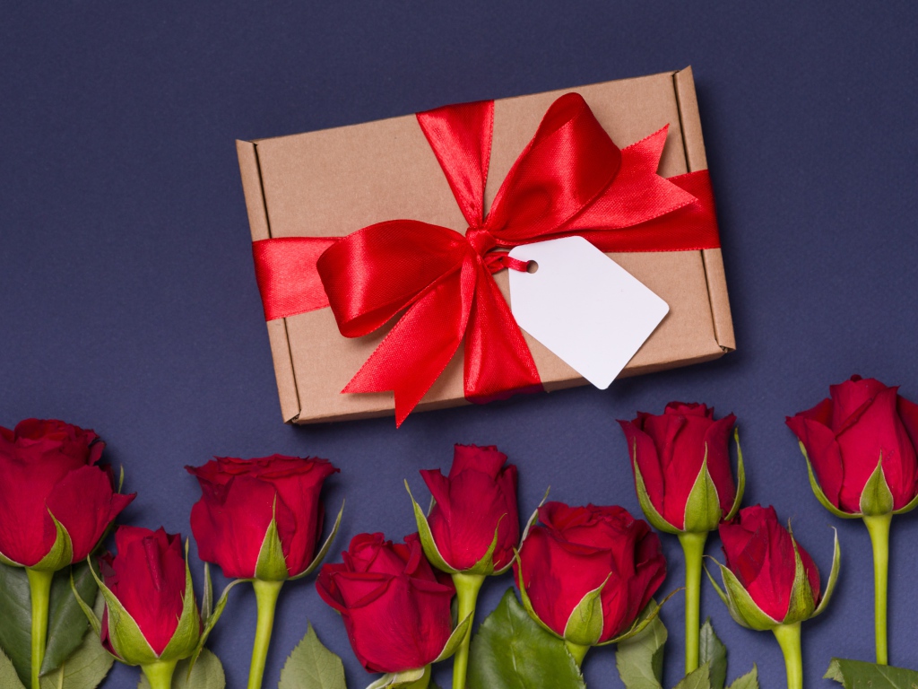 Подарок с красным бантом на столе с розами