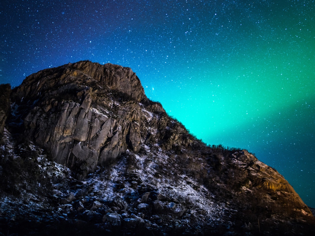 Красивое зеленое полярное сияние в звездном небе над горой 