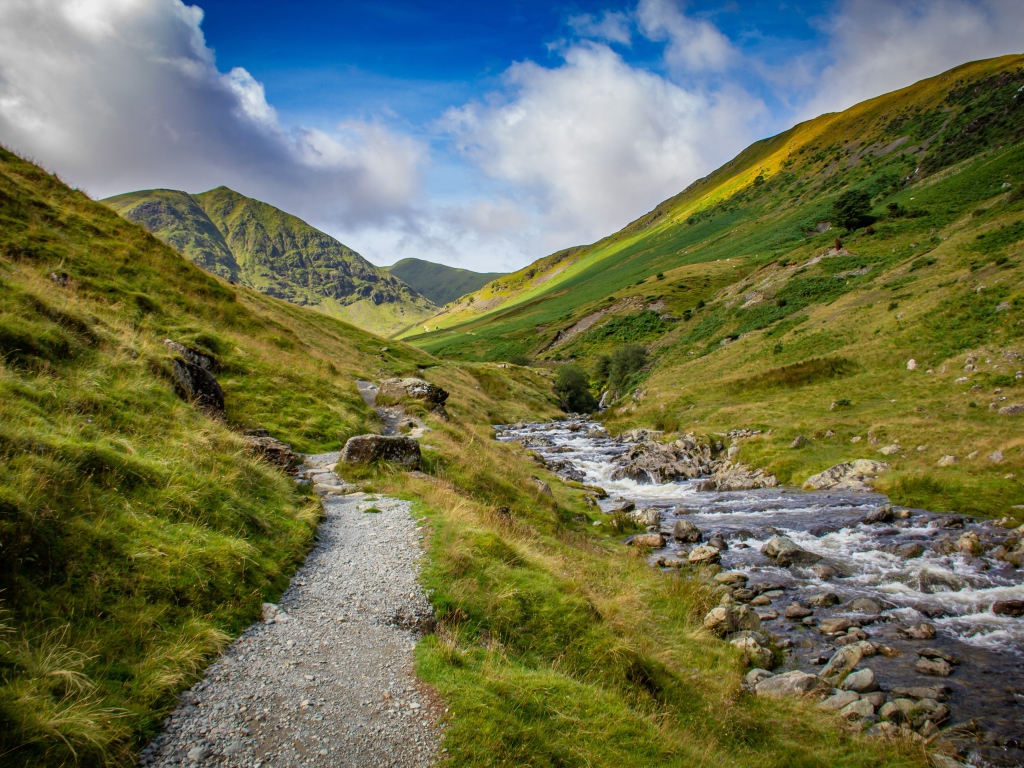 Тропа у реки на фоне покрытых зеленью гор 