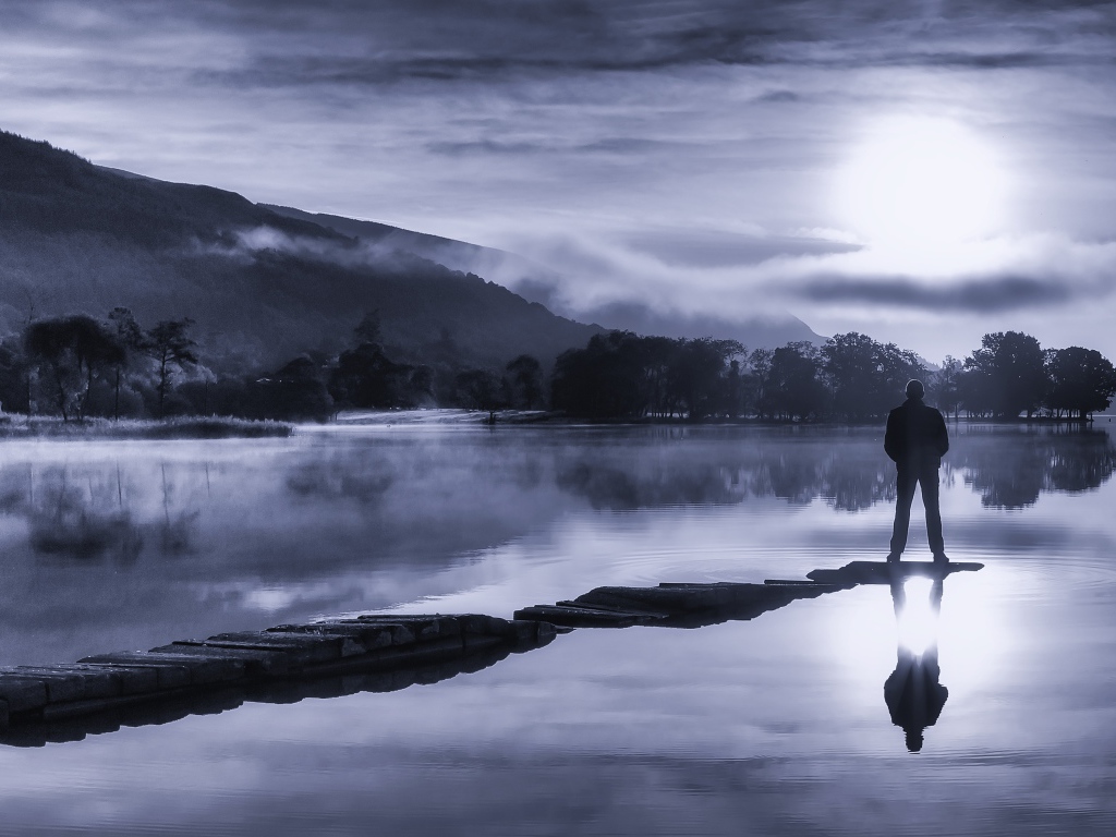 Мужчина стоит на мосту у озера ночью при свете луны