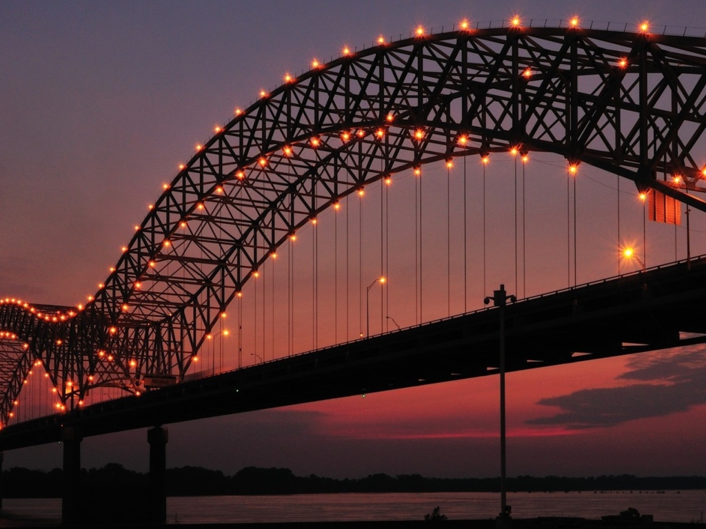 Арки на железном мосту с фонарями ночью через реку 