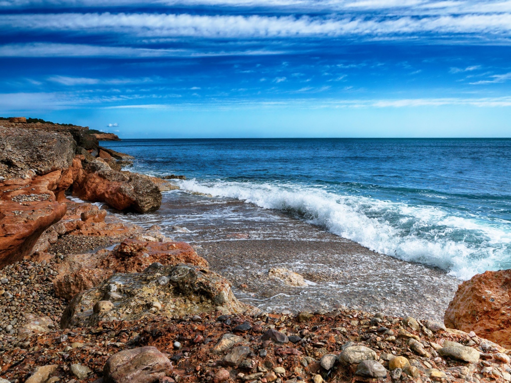 White waves by the sea with large stones under a blue sky