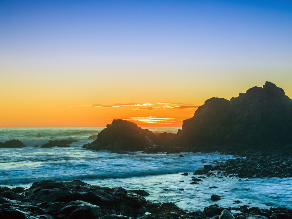 Закат солнца над океаном с камнями на берегу 