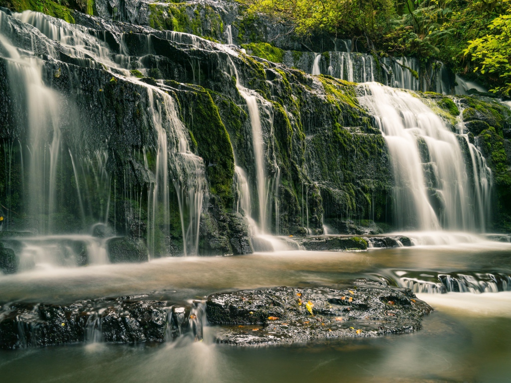 Водопад в лесу стекает по покрытым мхом камням 